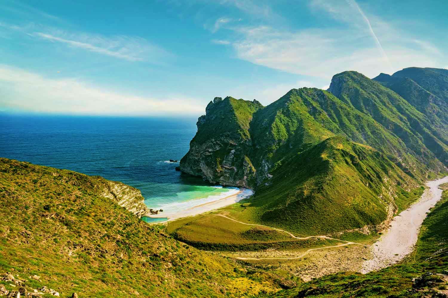 Lush green mountains with hidden beach cove and turquoise waters in Oman's coastal landscape